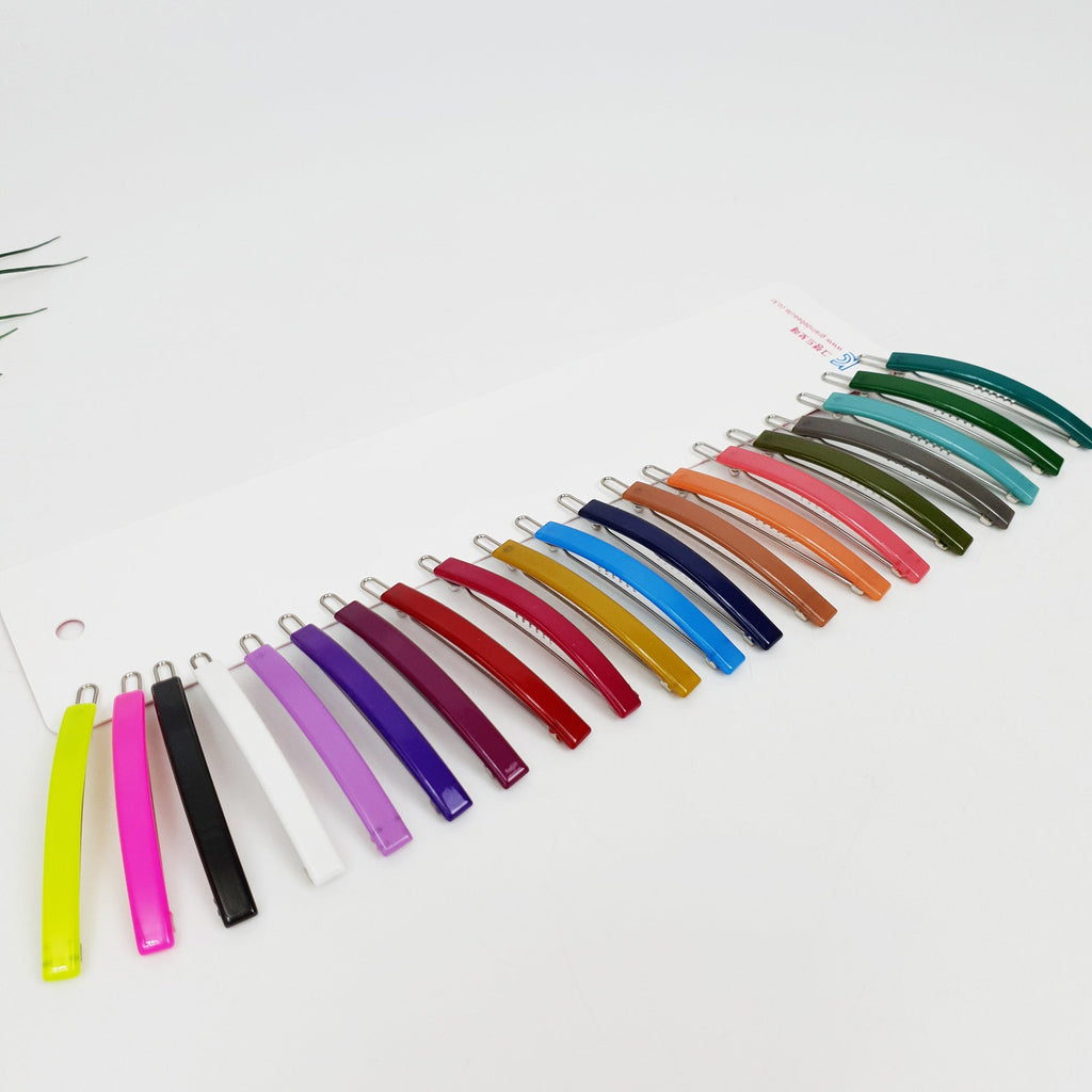 Slim rectangular cellulose acetate hair slide in vivid red. Minimalist straight bobby pin for side bangs, glossy hair accessory for thin hair. A set of twenty hair clips in various colors including green, blue, red, purple, pink, yellow, orange, brown, and white. The clips are arranged in a row on a white surface.
