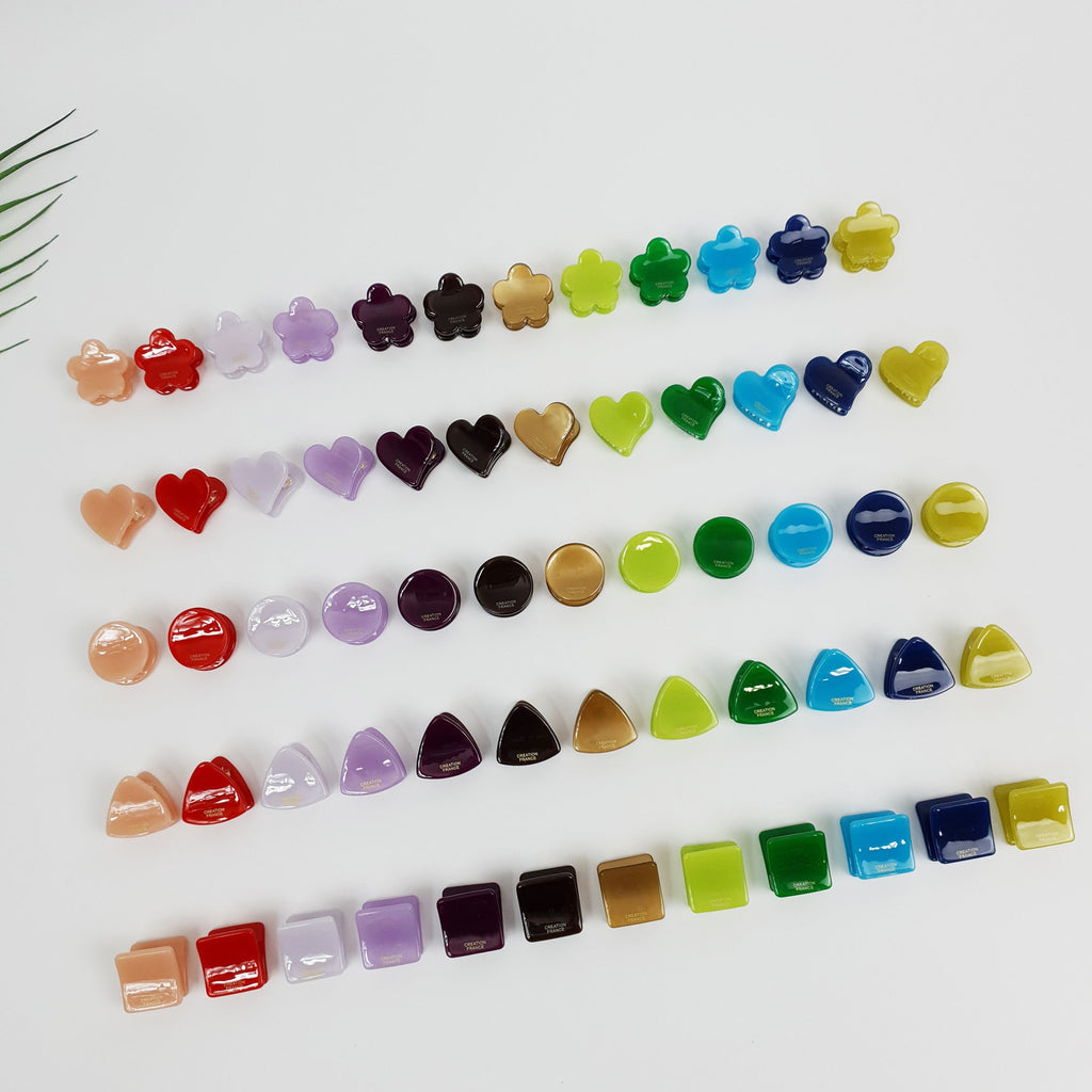 Tiny flower shaped cellulose acetate hair claw in vivid red. Mini geometric hair clip set (heart, circle, triangle, square) for styling bangs, Y2K colorful accessory. A collection of colorful plastic hair clips in various shapes, including flowers, hearts, circles, and triangles. The clips are arranged in rows on a white surface.