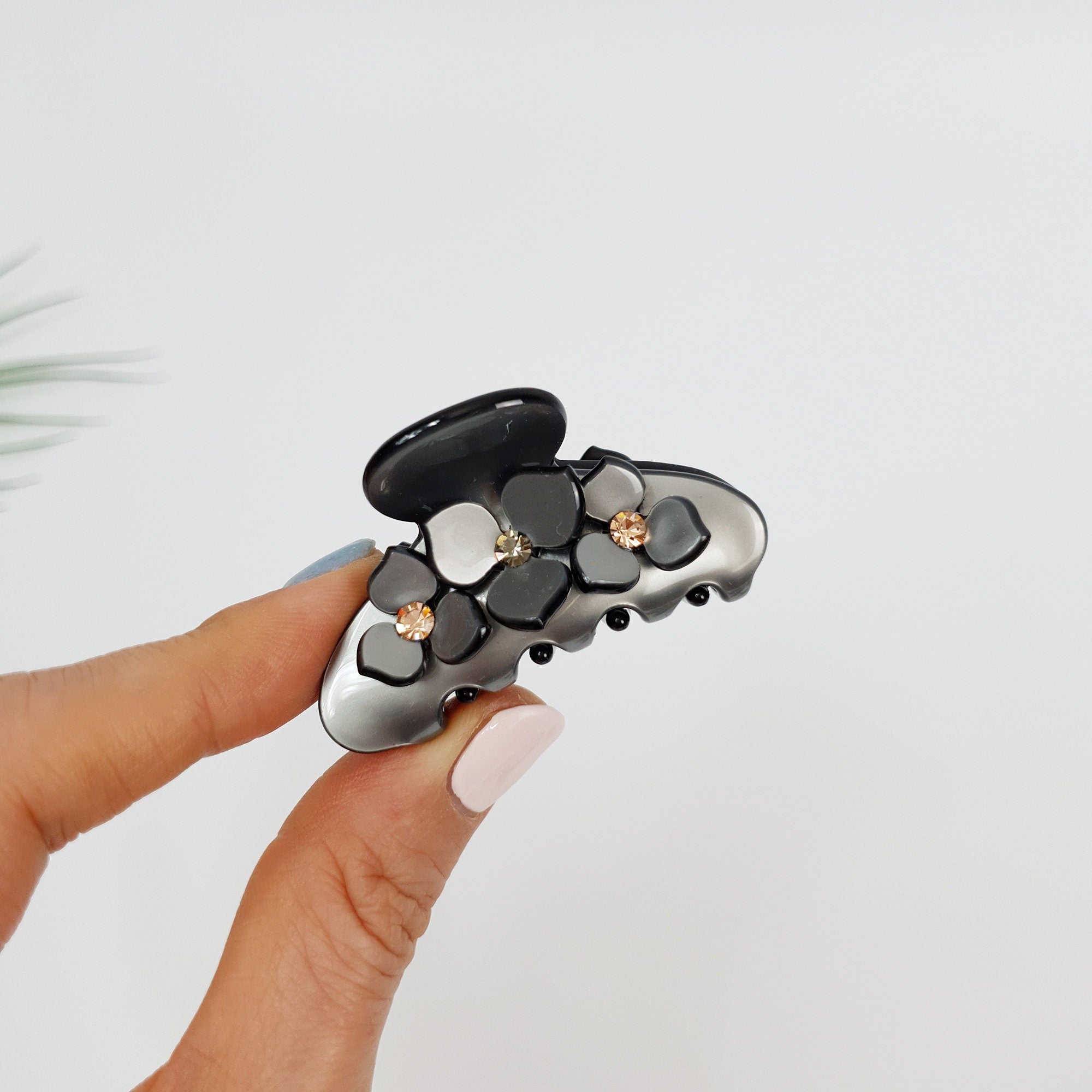 Small cellulose acetate flower hair claw with rhinestone accents. Pastel floral hair clip for half up hairstyles. Cute Korean accessories gift. A black and silver hair claw with a floral design. The claw has a silver base with black accents and is decorated with white, gray, and black flowers with small rhinestones in the center of each flower.