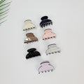 Mini acetate hair claw clips in pastel colors. Small half moon jaw clips for styling bangs or side hair. Tiny decorative hair accessories for women and toddlers.  Seven plastic hair clips in various colors including black, white, brown, pink, and light purple. The clips are all the same shape and size, with a rounded top and four prongs on the bottom.