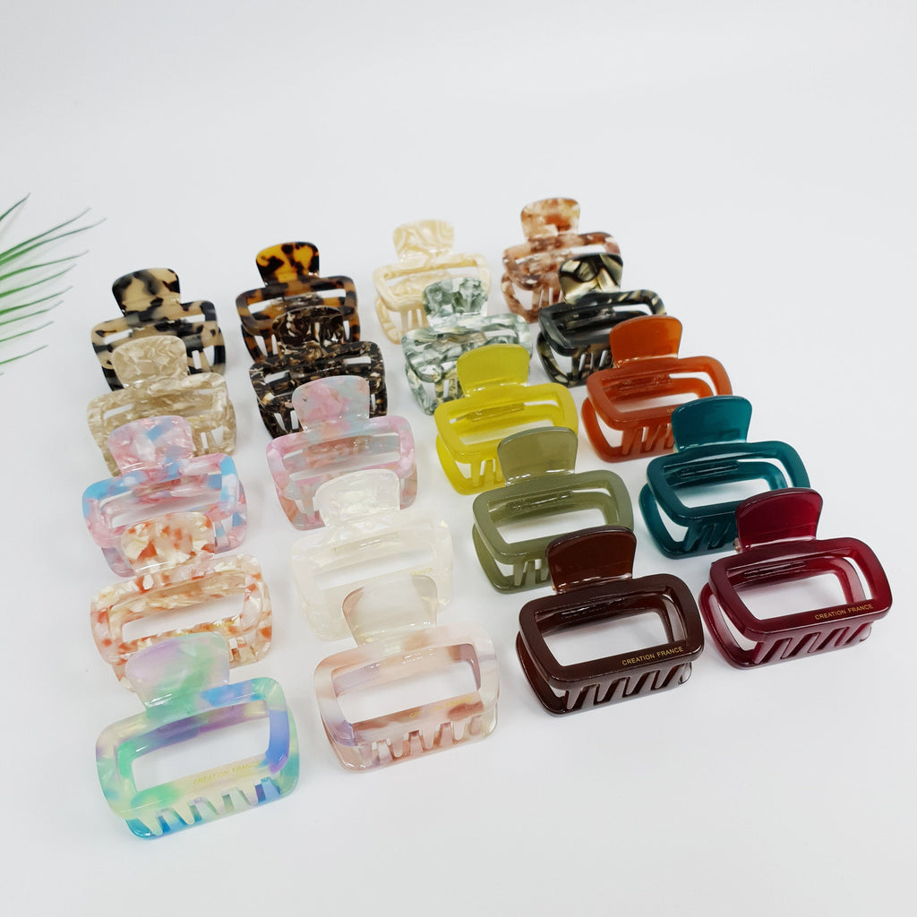 Cellulose acetate rectangular frame hair claw clip in tortoise shell and solid colors. 2 inch geometric open shape jaw clamp for half-up hairstyles. A collection of assorted hair clips in various colors and patterns. The clips are made of plastic and have a variety of designs, including floral, geometric, and abstract patterns. The clips are arranged in a row on a white surface. Some of the clips have the words 'CREATION FRAME' printed on them.