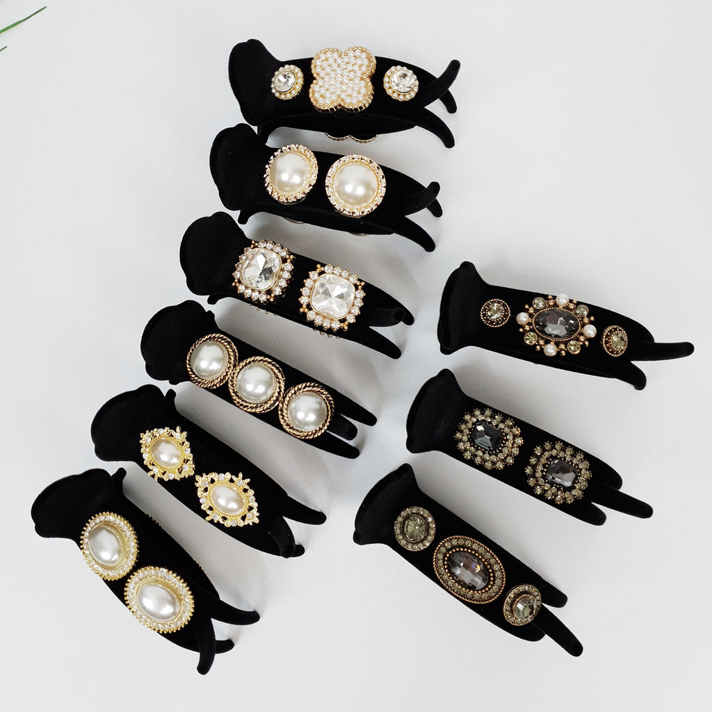 Black velvet circular hair claw clip with pearl and rhinestone embellishments. 3.1 inch round bun holder clamp for elegant updo hairstyles. A collection of hair clips with various designs, including pearl, rhinestone, and floral accents. The clips are displayed on black velvet stands against a white background.
