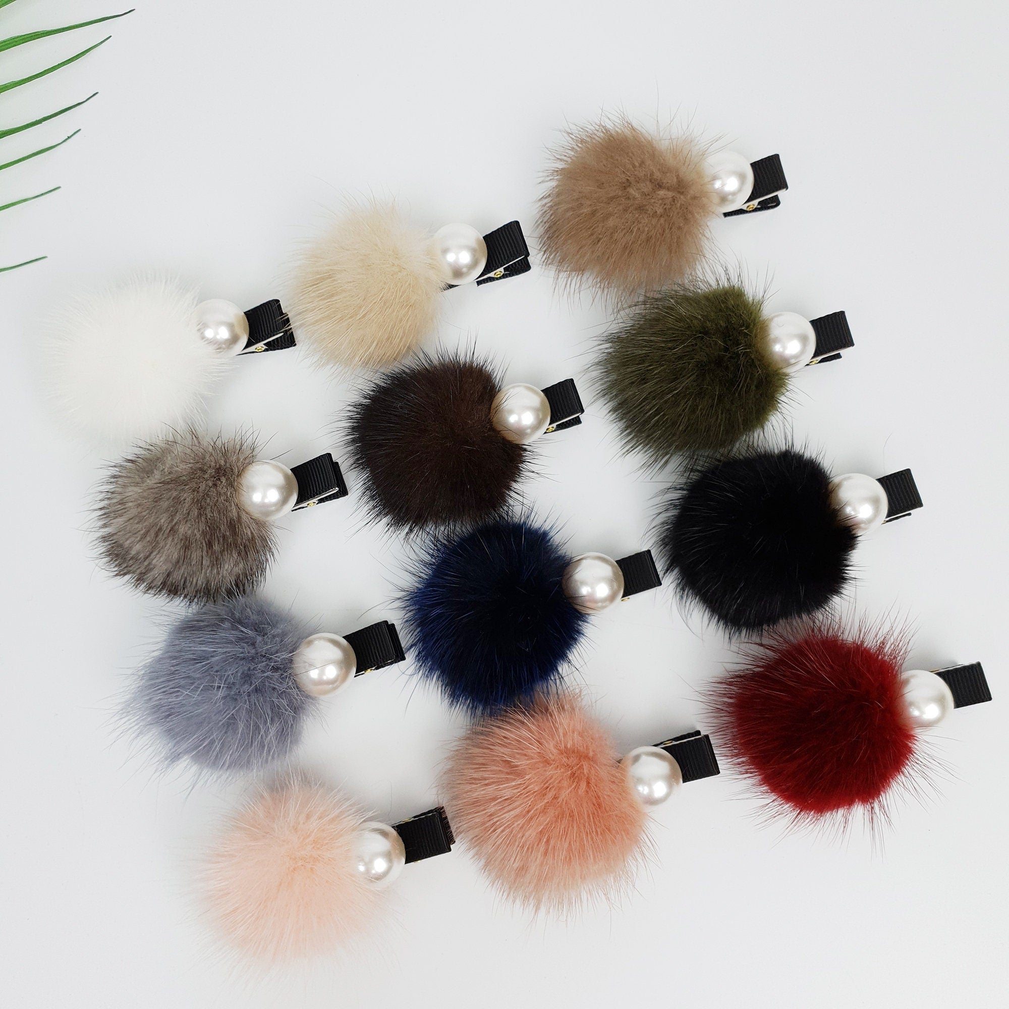 Real mink fur pom pom hair clip with pearl accent. Soft fluffy winter hair accessory for girls and women. Ribbon wrapped alligator clip for side bangs.  Twelve faux fur pom pom hair clips with pearl accents. The pom poms are in various colors including white, brown, gray, green, blue, pink, and red.