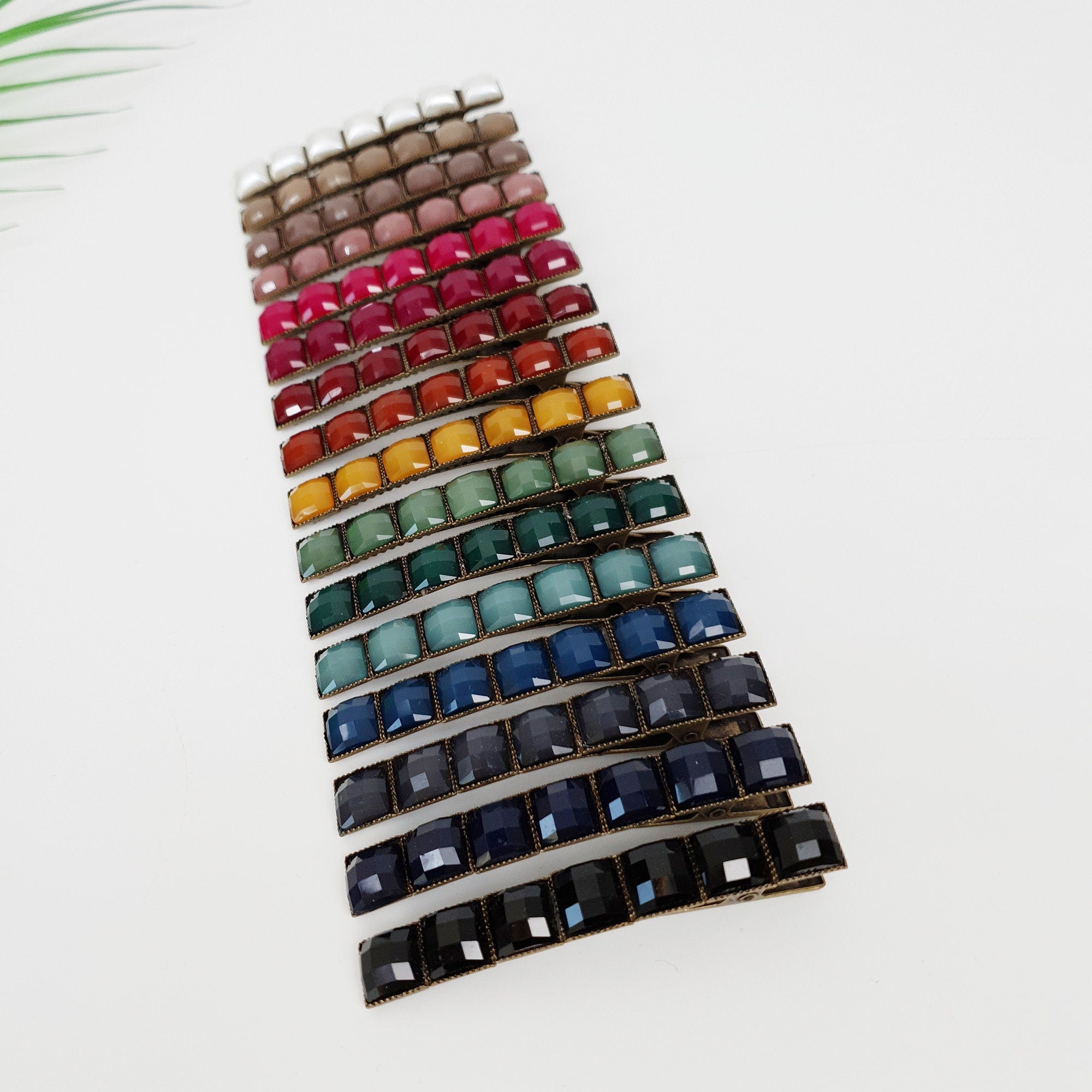 Vintage antique style Formica mini square hair claw clip with crystal-like finish. 2.4 inch geometric barrette for women's side hair styling. Retro Korean fashion accessory. A set of 18 hair clips with a rainbow of colors. The clips are made of metal and have a row of square-shaped rhinestones. The colors of the rhinestones are white, beige, pink, red, orange, yellow, green, teal, blue, navy, black, and gray.