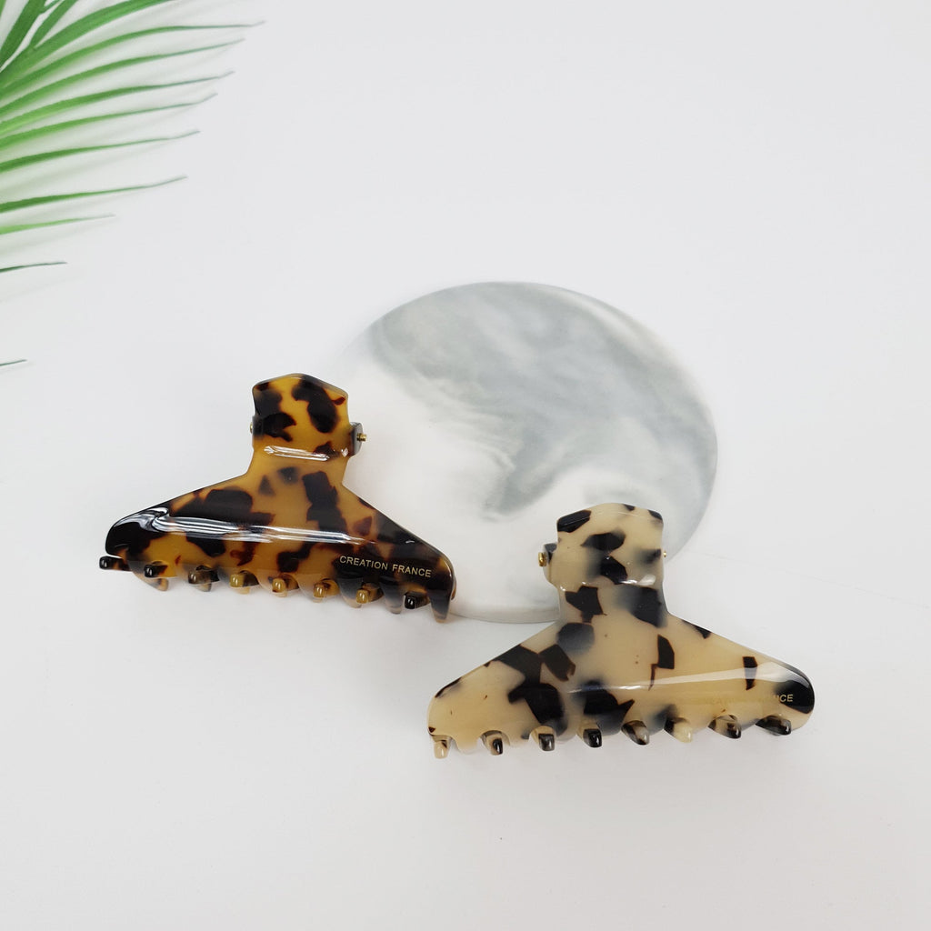 Cellulose acetate hair claw clip in tortoise shell pattern with an open triangle design. Medium 2.8 inch jaw clip for half-up hairstyles. Two tortoise shell hair clips. The hair clips are made of plastic and have a brown and black pattern. The hair clips are on a white surface. The larger hair clip has the words 'CREATION FRANCE' printed on it.