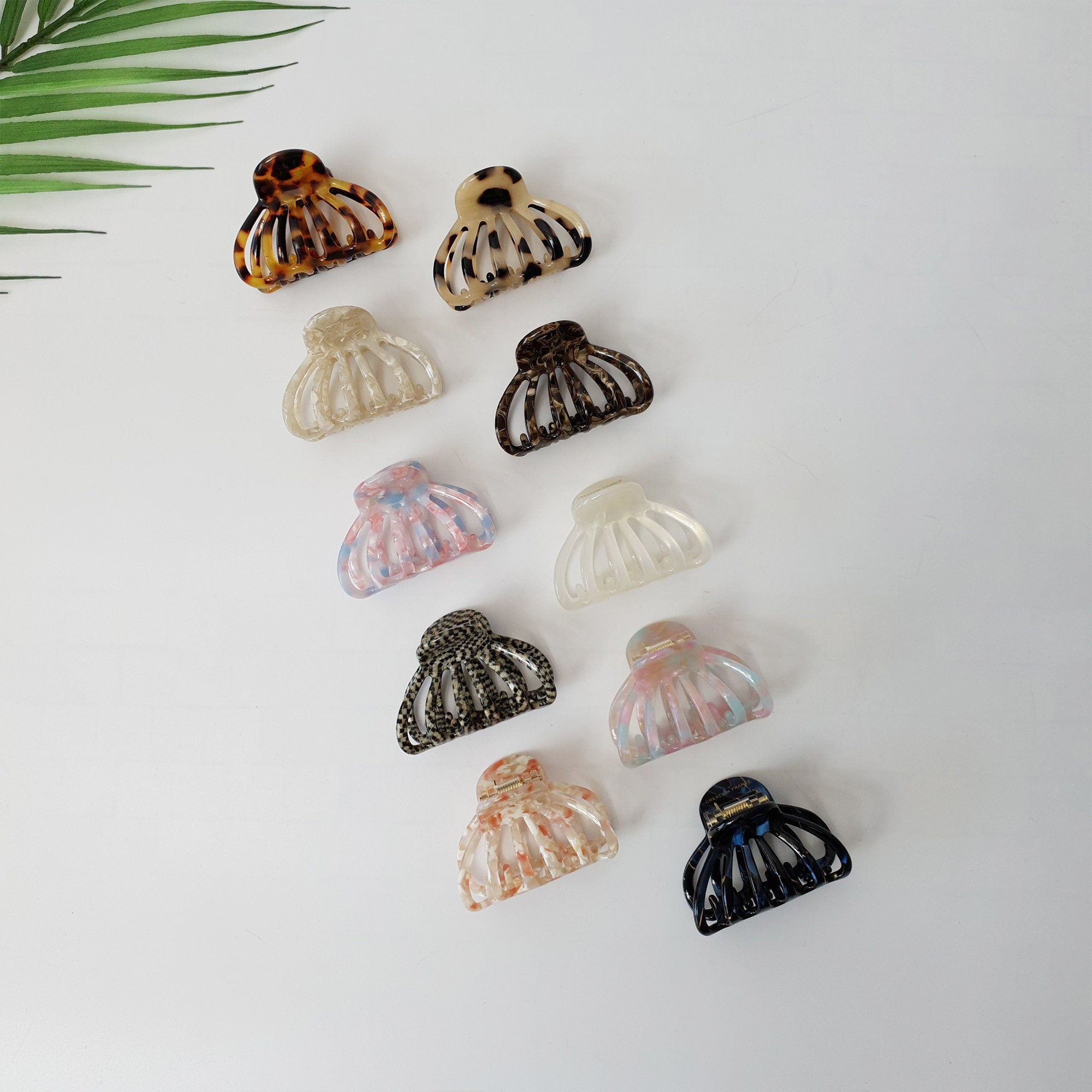 Cellulose acetate small hair claw clip in tortoise shell and marble patterns for half up hairstyles, round shell shape jaw clip for women. A collection of ten assorted plastic hair clips. The clips are in various colors and patterns, including brown, black, white, and pink. The clips are all in the shape of a half-circle with four prongs on each side.