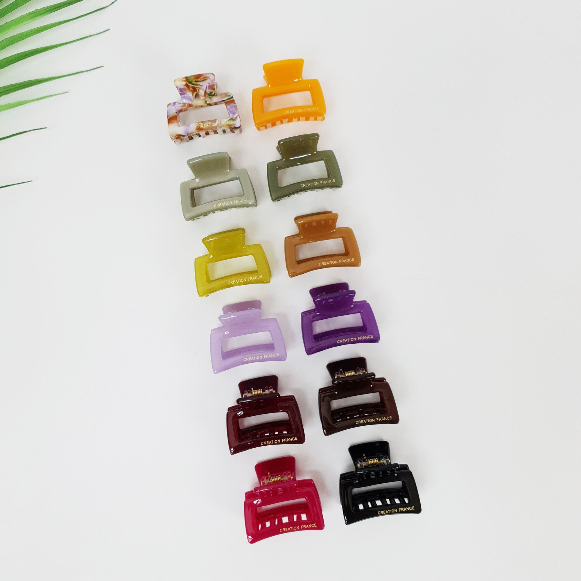 Cellulose Acetate Small Square Hair Claw Clip 1.5 inch Minimalist Geometric Design for Half Updo A set of twelve hair clips in various colors including purple, green, yellow, red, black, and brown. Each clip has a rectangular shape with a small opening in the center and the words 'CREATION FRANCE' printed on the bottom.