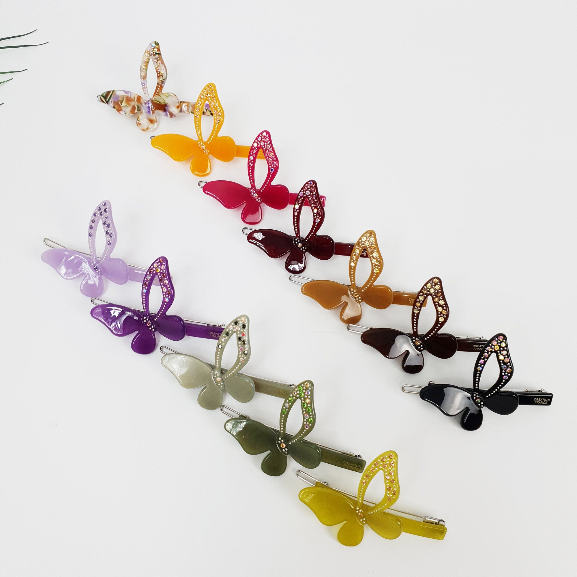 Cellulose Acetate Butterfly Hair Barrette with Rhinestones 2.6 inch Cute Side Bangs Clip A collection of butterfly hair clips in various colors including purple, green, red, orange, and brown. The clips are all made of plastic and have a shiny finish. They are arranged in a row on a white background.