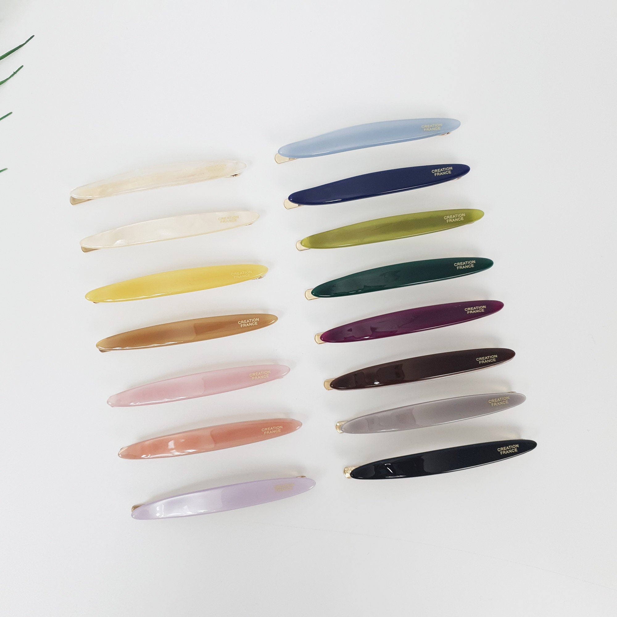 Pastel acetate oval hair slide with gold snap base, minimalist glossy barrette for side bangs styling, cute hair accessory for women. A set of 14 hair clips in various colors, including light blue, white, yellow, brown, pink, purple, green, dark green, dark purple, maroon, gray, and black. Each clip has a curved shape and features the text 'CREATION FRANCE' in gold lettering.