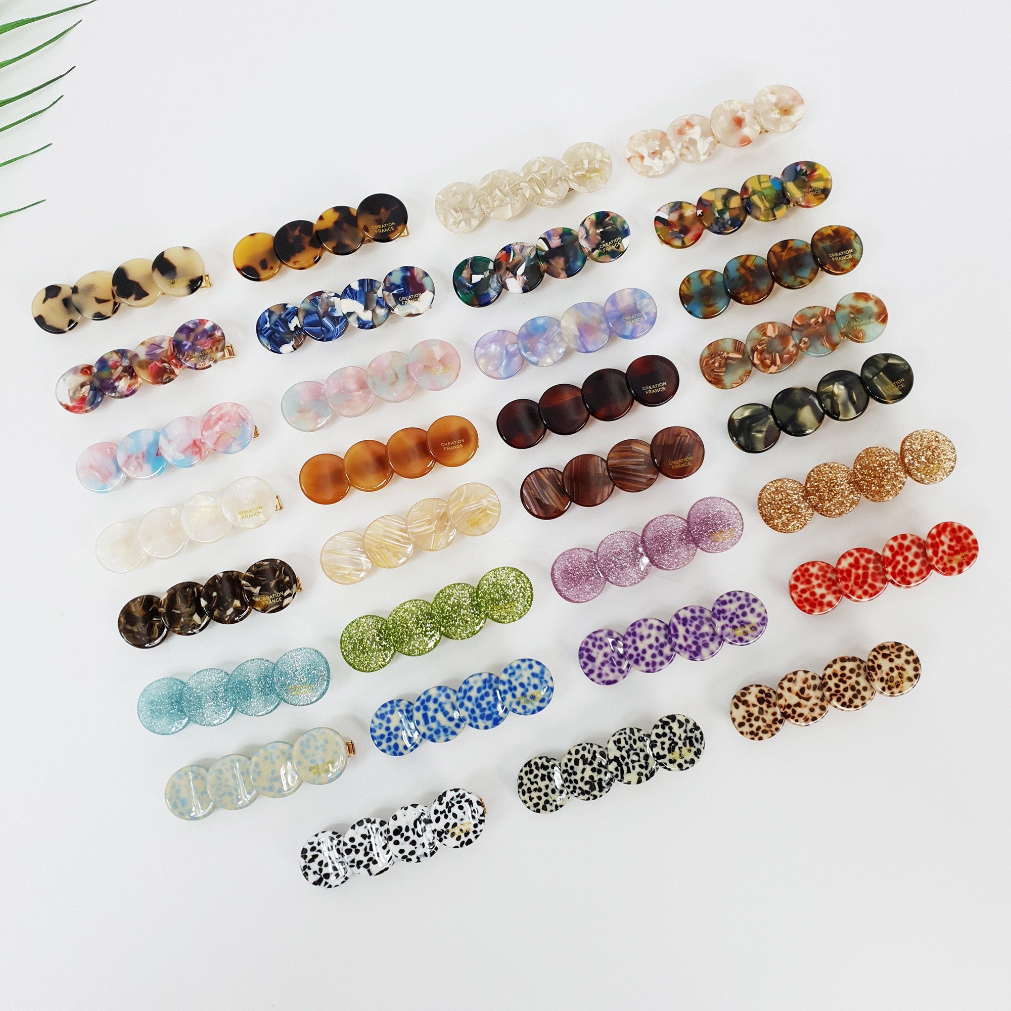 Cellulose acetate petal hair clip in tortoise shell and marble patterns. Vintage style geometric alligator clip for side bangs. Cute retro hair accessory gift for her. A collection of 20 assorted hair clips with various patterns and colors including blue, green, brown, red, purple, and white. The clips are made of plastic and have a round shape.