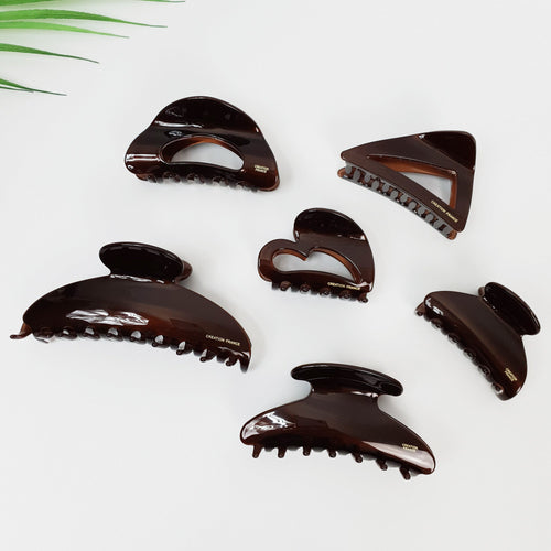 Chic brown cellulose acetate hair claw clips in geometric shapes including heart triangle and half moon, minimalist hair accessories for women. Six brown plastic hair clips with a gold inscription that reads 'CREATION FRANCE'. The hair clips are in various shapes, including a heart, a triangle, and a rounded rectangle.