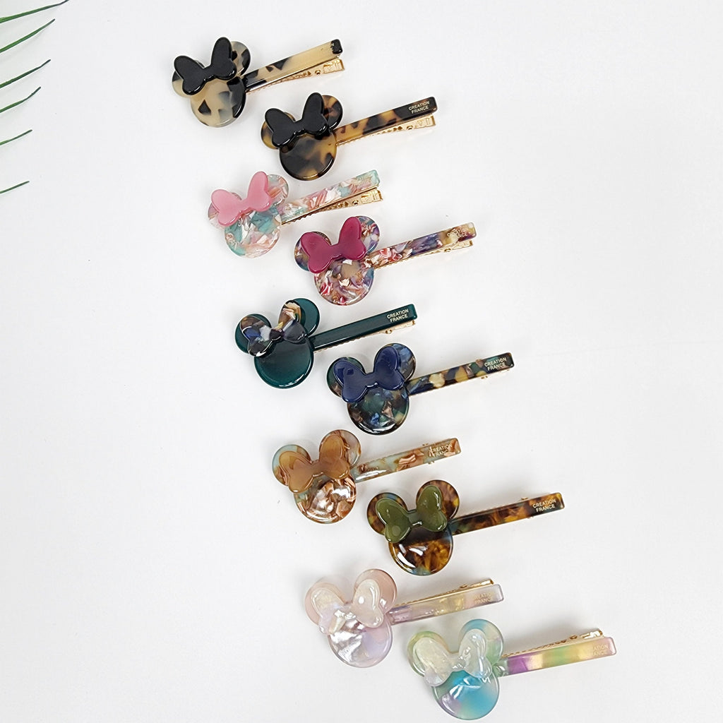 Small cellulose acetate mouse ear hair clip with bow. Tortoise shell and pastel marble alligator clamp. 2.7 inch cute side pin for bangs and girls. Assortment of colorful hair clips with a cartoon mouse design. The clips are made of plastic and have a gold metal clip. The clips are arranged in a row on a white background.