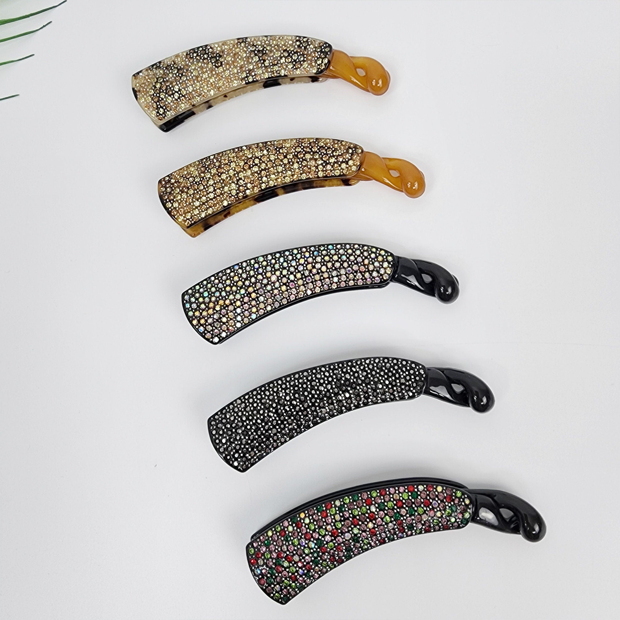 Medium cellulose acetate banana clip with rhinestone pave. Tortoise shell and black crystal ponytail holder. 4.3 inch luxury hair accessory for half updos and weddings.  Five hair clips with a curved shape. The clips are decorated with rhinestones in various colors, including black, white, and iridescent. The clips are arranged vertically, with the top clip being a brown and white leopard print.
