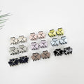 Set of 2 mini cellulose acetate three-leaf clover hair claw clips. Pastel shamrock jaw clamps with rhinestone center. 0.8 inch tiny accessories for bangs and side hair. Twelve pairs of clover-shaped hair clips in various colors including black, brown, light pink, light blue, and yellow. The clips are arranged in rows on a white surface.
