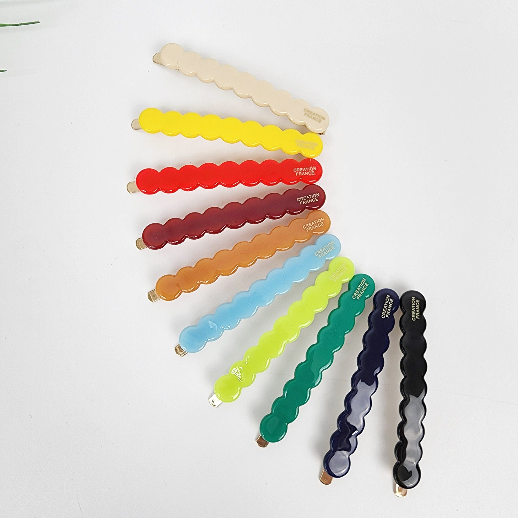 Cellulose acetate wavy bobby pin in vivid colors, scalloped hair slide for side bangs, cute minimalist hair clip for women. Ten hair clips in various colors including cream, yellow, red, maroon, orange, light blue, lime green, dark green, navy blue, and black. Each clip has a wavy design and the words 'CREATION FRANCE' printed on the side.