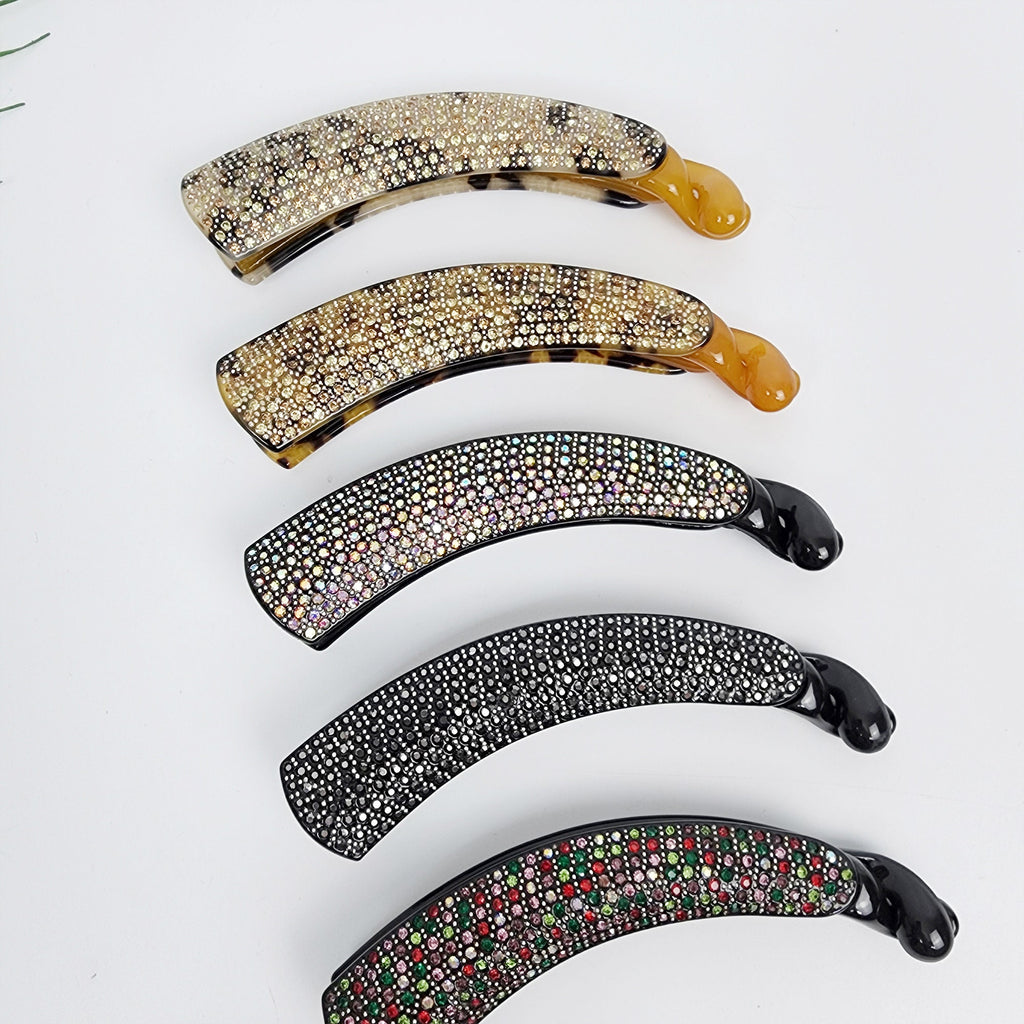 Cellulose acetate banana clip with rhinestones. Large 4.9 inch sparkly hair comb for secure ponytails and updos.  Four decorative hair clips with rhinestones. The clips are curved and have a shiny finish. The clips are in different colors, including black, brown, and clear.