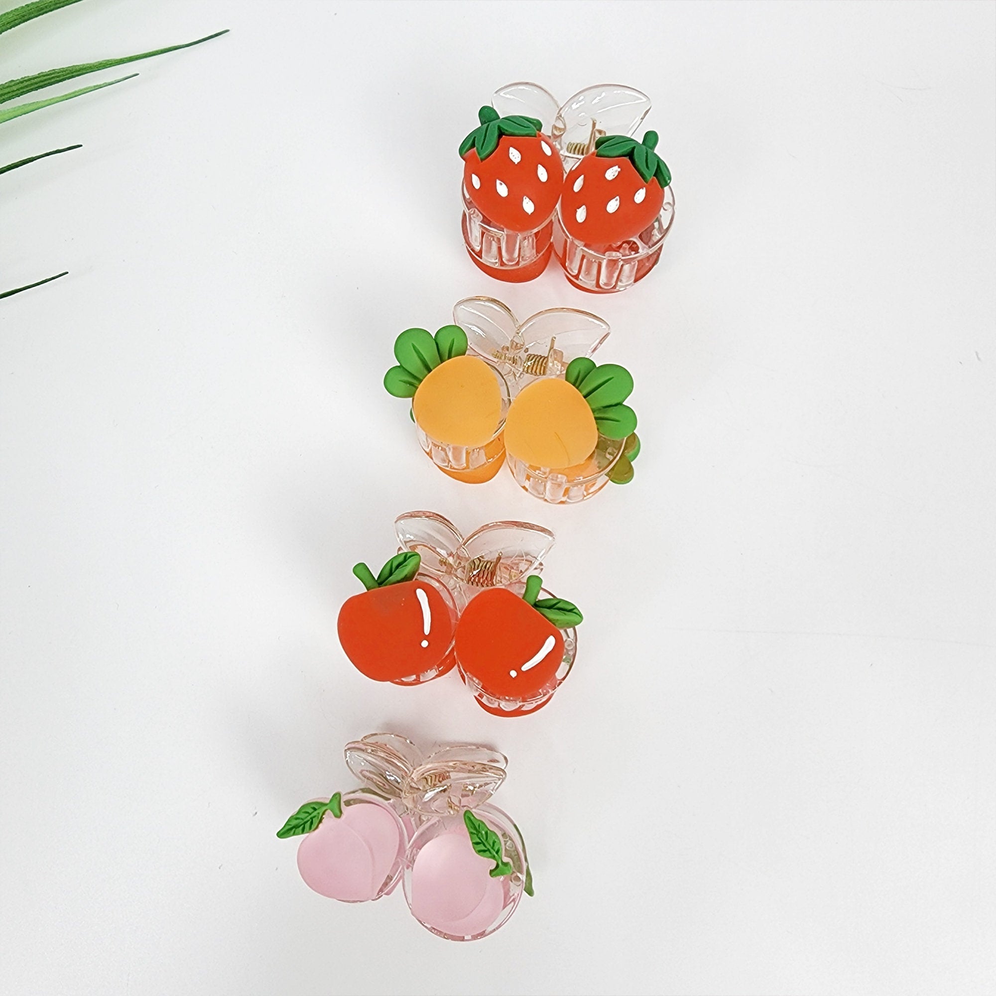 Transparent mini hair claw clip with colorful fruit charms strawberry carrot apple peach for playful summer hairstyles.  Four sets of fruit-shaped hair clips. The first set is red strawberries, the second set is orange peaches, the third set is red apples, and the fourth set is pink peaches.