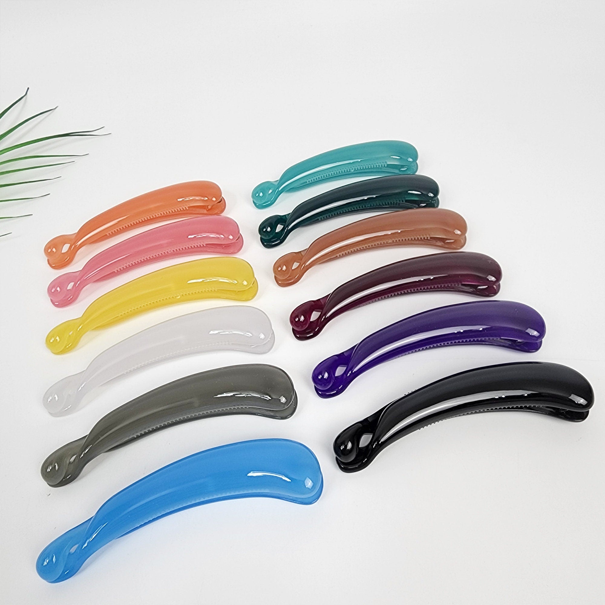 Cellulose acetate curved banana hair clip in solid glossy colors, minimalist ponytail holder with inner teeth for half-up styling. A set of 14 hair clips in various colors including light blue, dark blue, gray, black, purple, maroon, brown, orange, yellow, white, pink, and light pink. The clips are all made of a smooth, shiny plastic and have a curved shape.