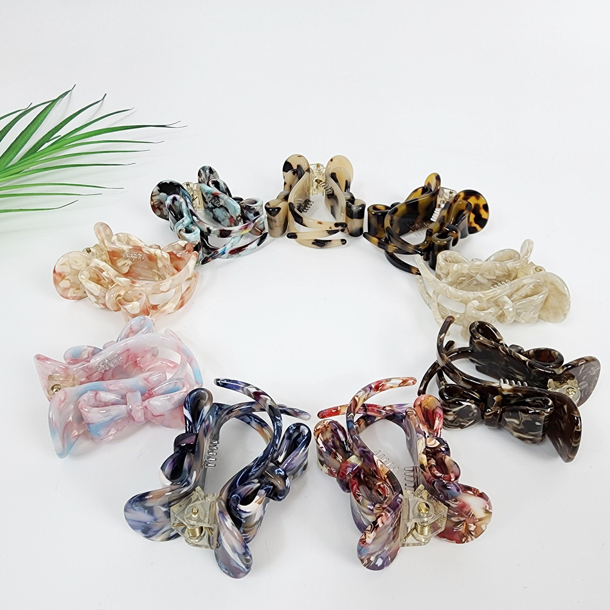 Cellulose acetate mini claw clip with bow design, 2 inch round hair clamp for half-up styling and ponytails. A collection of eight colorful hair clips with various patterns. The clips are made of plastic and have a claw design. The clips are arranged in a circle on a white background.