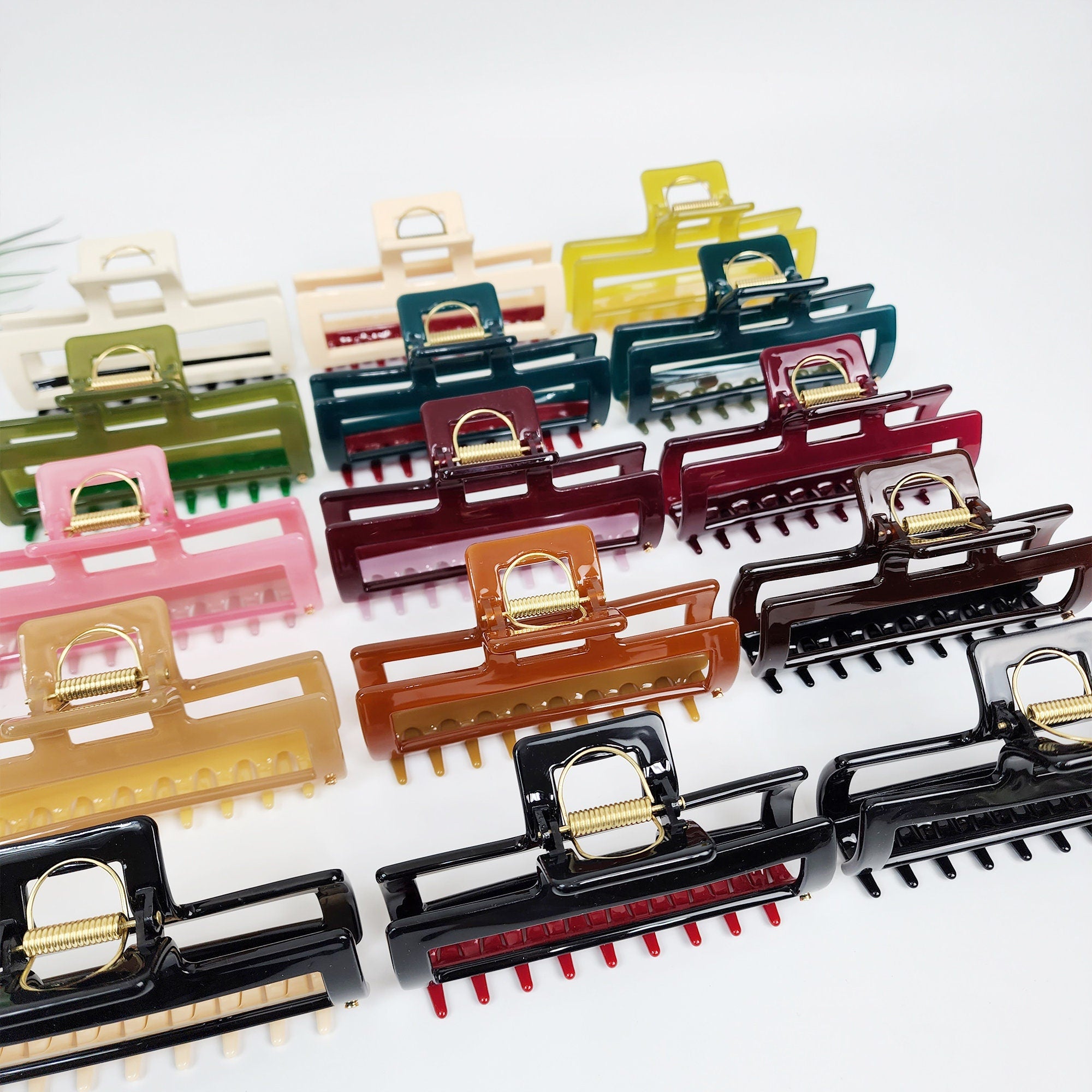 Large 4.7 inch cellulose acetate rectangular hair claw clip with durable U-wire spring. Big geometric jaw clip ideal for securing thick hair in french twist or bun hairstyles. A collection of colorful hair clips in various colors including pink, green, brown, red, black, and yellow. The clips are made of plastic and have a spring mechanism to hold hair in place. The clips are arranged in rows, with the largest clips at the bottom and the smallest clips at the top.