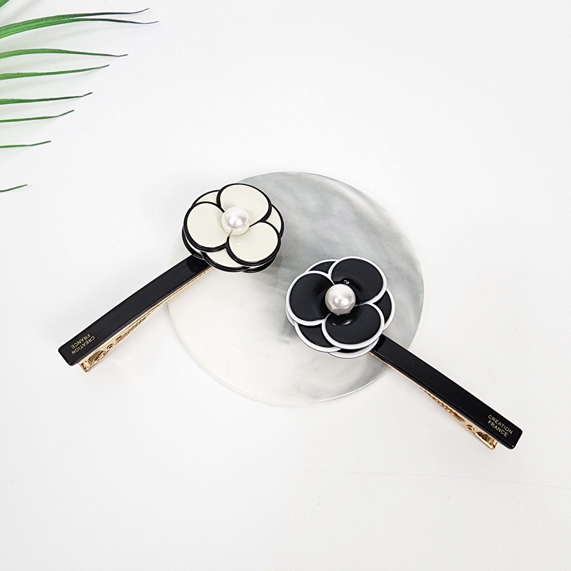 Elegant acetate pansy flower hair clip with pearl center, black and white floral side barrette for women, sturdy Korean style hair accessory for birthday gift. Two black and white flower hair clips with a pearl in the center of each flower. The clips are on a white marble surface. The text on the clips reads 'CREATION FRANCE'.