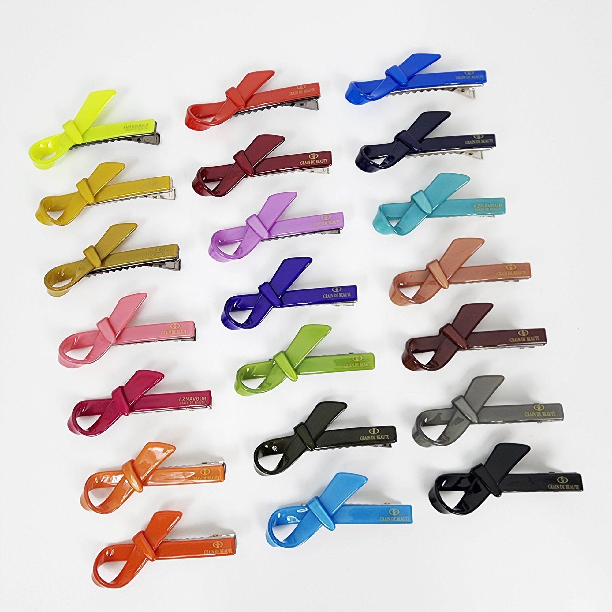 Cellulose acetate bow hair clip in solid vivid colors small beak barrette for women and girls side bangs Twenty hair clips with a bow design in various colors including yellow, orange, red, pink, purple, blue, green, brown, gray, and black. The clips are all made of plastic and have a gold logo that reads 'GRANDE BEAUTÉ'.