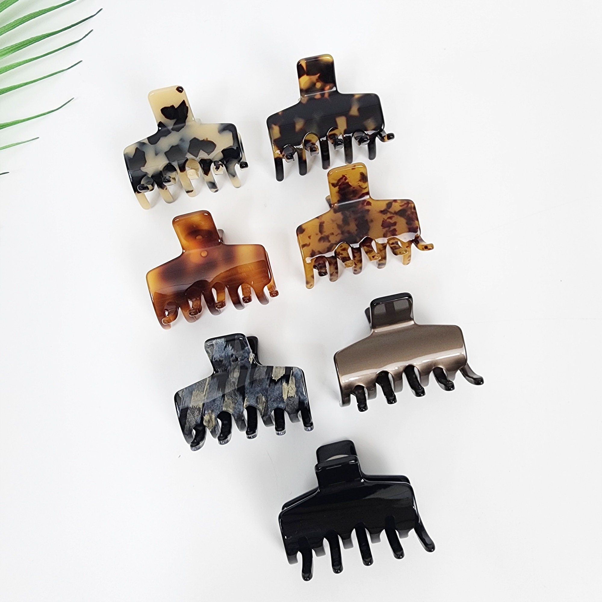 Cellulose acetate square hair claw featuring classic tortoise shell pattern and minimalist design. Small 2 inch jaw clip perfect for half up hairstyles and fine hair securing. Six different hair clips in various patterns and colors. The clips are made of plastic and have a claw shape. The clips are in the following colors: brown, black, and gray. The clips are arranged in a row on a white surface.