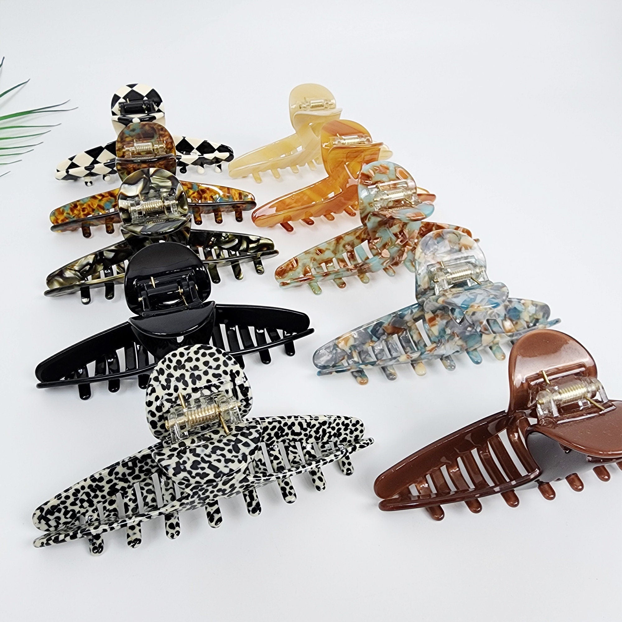 Large cellulose acetate twist claw clip in tortoise shell and checkerboard patterns for securing thick hair updos. A set of eight hair clips in various colors and patterns. The clips are made of plastic and have a variety of shapes and sizes. The clips are arranged in a row on a white surface. The clips are all different colors and patterns, including black and white, brown, blue, and green. The clips are all designed to hold hair in place.