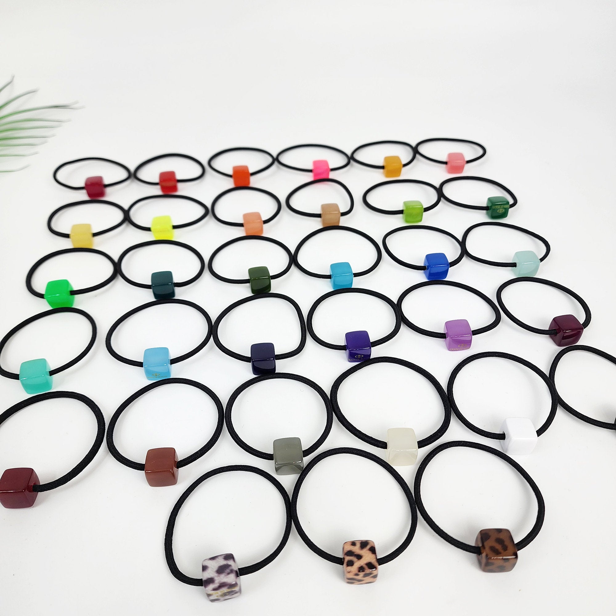 Cellulose acetate mini cube hair tie in 33 vivid colors including neon, pastel, and tortoise shell. Small square geometric ponytail holder for toddlers and women. A collection of 30 colorful hair ties with square-shaped beads. The beads are in various colors including red, orange, yellow, green, blue, purple, brown, black, white, and leopard print.