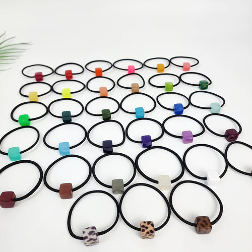 Cellulose acetate mini cube hair tie in 33 vivid colors including neon, pastel, and tortoise shell. Small square geometric ponytail holder for toddlers and women. A collection of 30 colorful hair ties with square-shaped beads. The beads are in various colors including red, orange, yellow, green, blue, purple, brown, black, white, and leopard print.