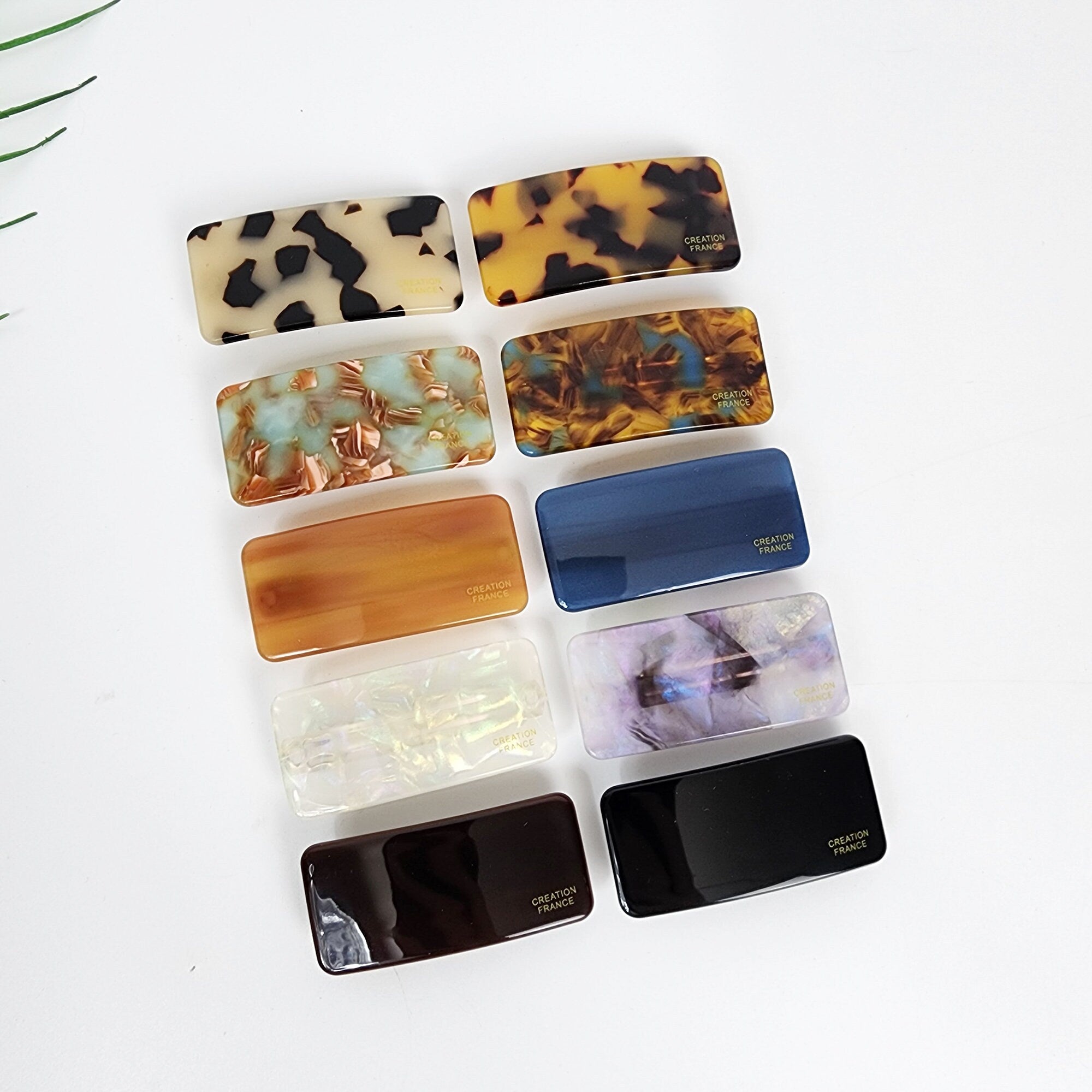 Cellulose acetate rectangle barrette in tortoise shell and pastel colors. Small 2 inch automatic hair clip for side bangs. Minimalist geometric hair slide.  Nine rectangular hair clips in various colors and patterns. The clips are made of plastic and have a smooth, glossy finish. The patterns include tortoise shell, marble, iridescent, and solid colors. The clips have the text 'CREATION FRANCE' printed on them.