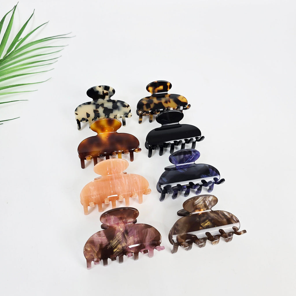 Cellulose acetate half moon hair claw clip in tortoise shell and peach, medium 2.4 inch jaw clamp for half up hairstyle. A set of seven hair clips in various colors and patterns. The clips are made of plastic and have a claw-like design. The colors include brown, black, purple, pink, and a mottled brown and gold pattern.