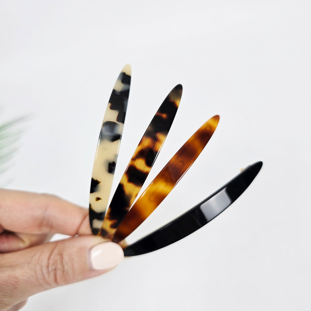 Cellulose acetate slim oval snap clip in tortoise shell and black, 3.1 inch long hair barrette, minimalist side bangs pin for women. Four hair clips in different patterns. One clip is black, one is brown and black, one is brown and white, and one is beige and black.