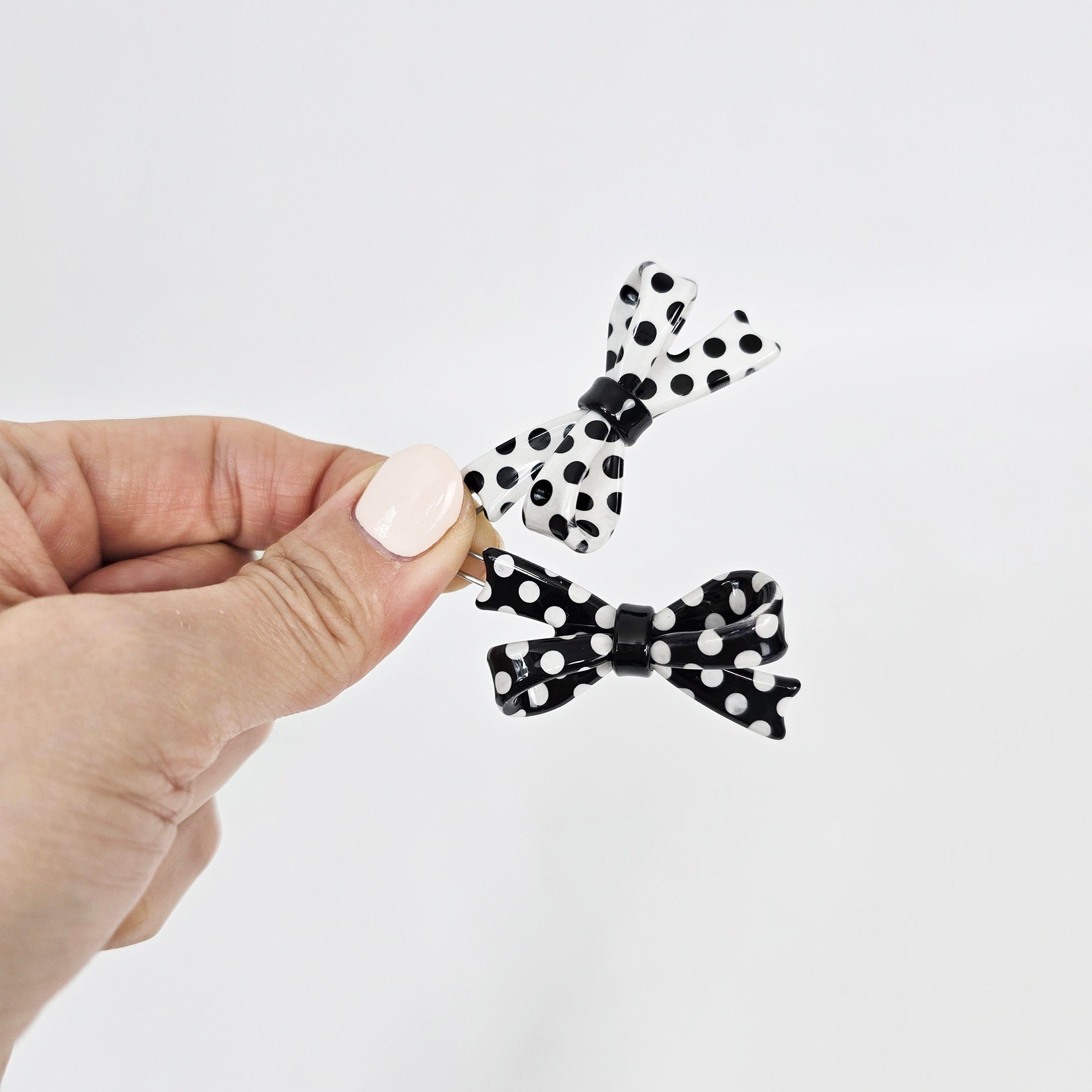 Cellulose acetate double bow hair clip with polka dot pattern, black and white snap barrette, cute mini hair pin for bangs and side hair. Two black and white polka dot bow hair clips. The bows are made of a shiny, translucent material.