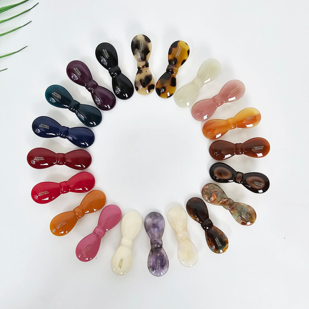 Cellulose acetate bow hair clip in tortoise shell and pink, small alligator clip for bangs, cute mini barrette for side hair. A collection of 17 assorted hair clips in various colors and patterns. The clips are all in the shape of a bow and are made of plastic. The colors include black, brown, white, pink, purple, and green. The patterns include solid colors, stripes, and polka dots.