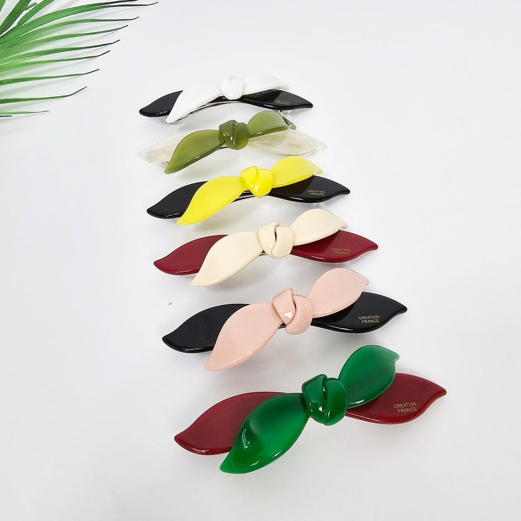 Cellulose acetate hair barrette featuring a two-tone double wave ribbon design in wine and beige. 3.7 inch automatic French clip, perfect for securing side bangs or half-up styles. A set of seven hair clips with bow designs. The clips are in various colors including white, green, yellow, pink, red, and black. Each clip has a small gold label with the text 'CREATION FRANCE'.