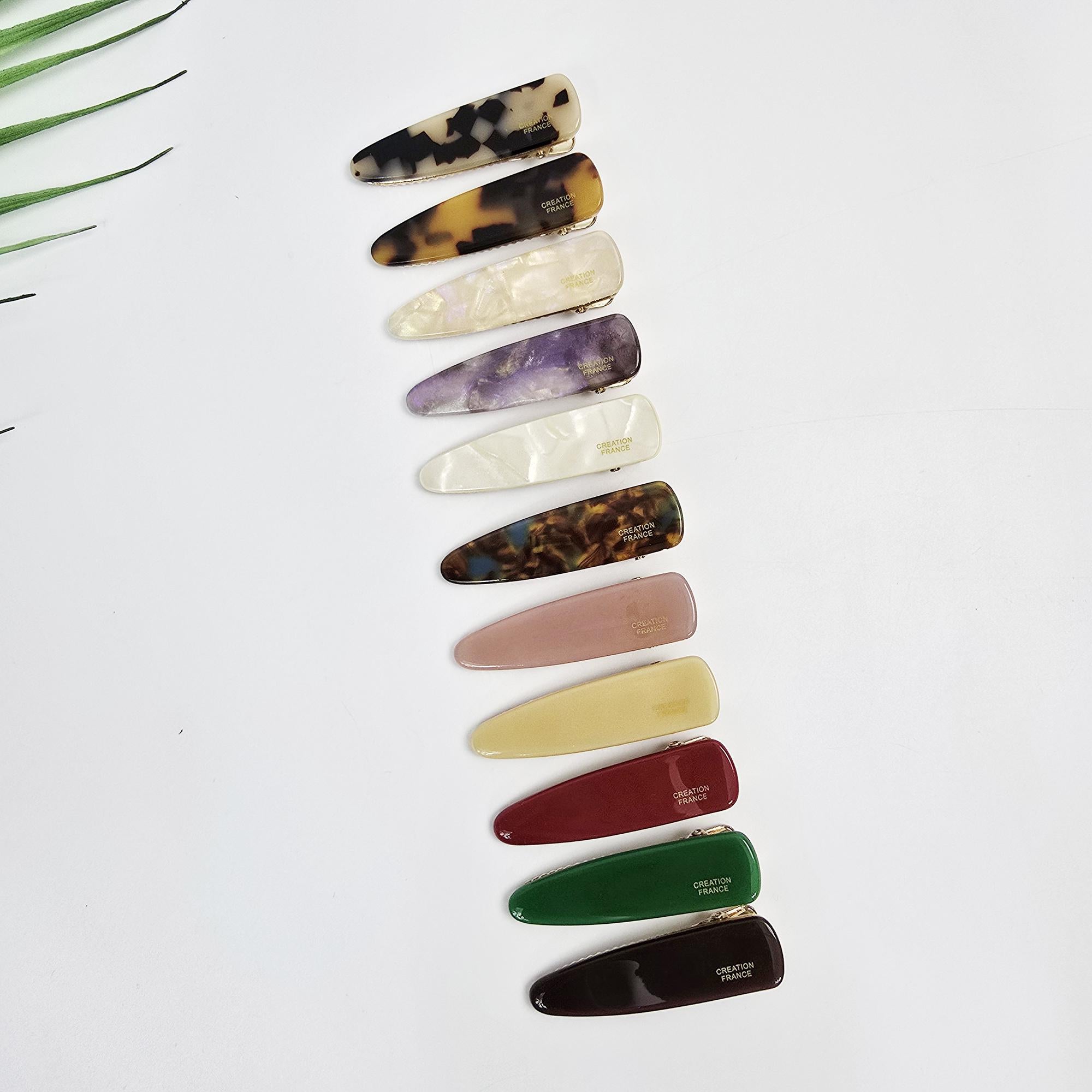 Small cellulose acetate hair clip featuring a slim triangle shape and alligator clip mechanism. Available in tortoise shell, pearl, and solid colors for pinning side bangs.