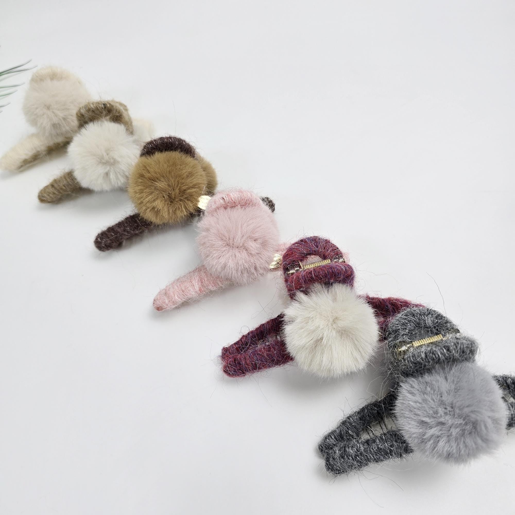 Large knitted hair claw clip wrapped in soft yarn with a faux fur pom-pom accent. 5.1 inch oversized jaw clip designed for holding thick hair updos. Cozy winter hair accessory available in beige and neutral tones.