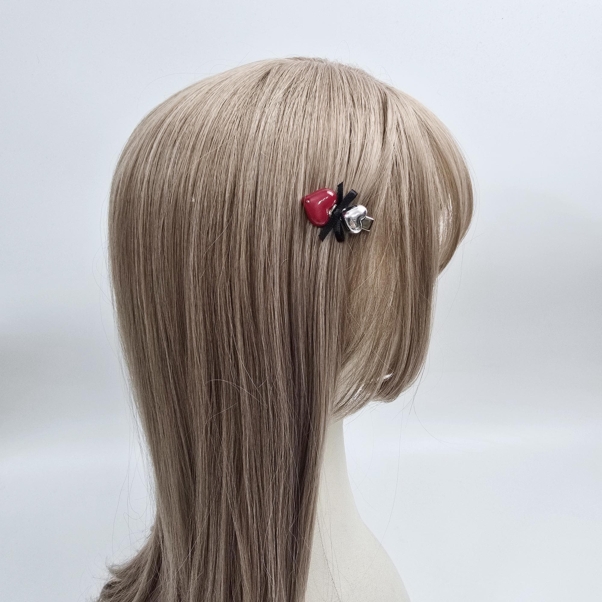 Cellulose acetate ultra mini hair clip featuring a glossy red heart and silver heart charm. 1.5 inch alligator barrette available with black ribbon bow. Cute valentine hair accessory for toddler girls. May include: A hair clip featuring a red heart and a black spider design. The clip is attached to a mannequin's light brown hair. The spider has a silver bell charm.  The hair clip is small and delicate, suitable for adding a touch of gothic or whimsical style to a hairstyle.