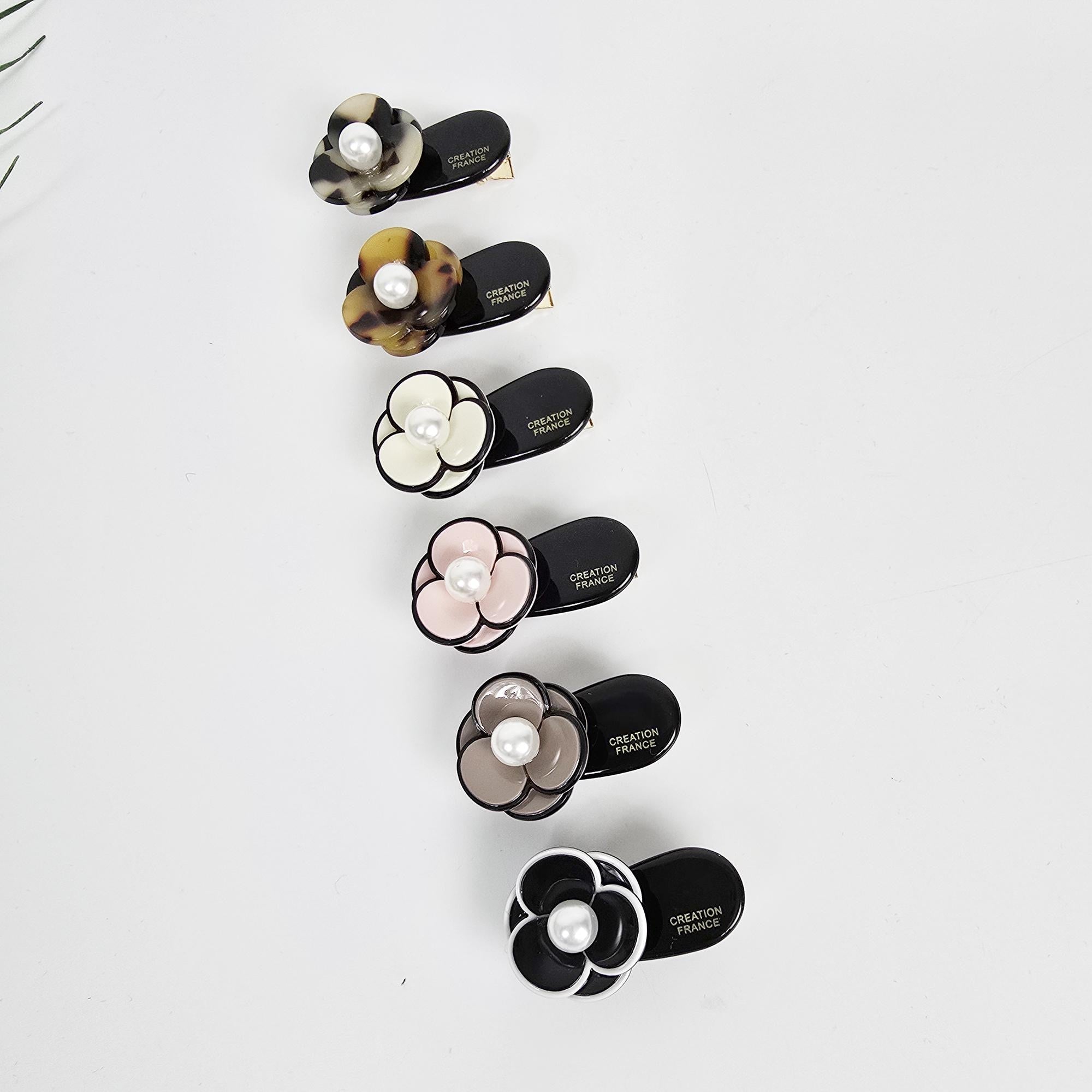 Cellulose acetate mini pansy flower hair clip with pearl center. Small 1.6 inch floral alligator barrette for toddlers and girls side hair. Six black hair clips with a pearl and flower design. The flowers are in various colors including white, brown, pink, and black. The clips are labeled 'CREATION FRANCE'.