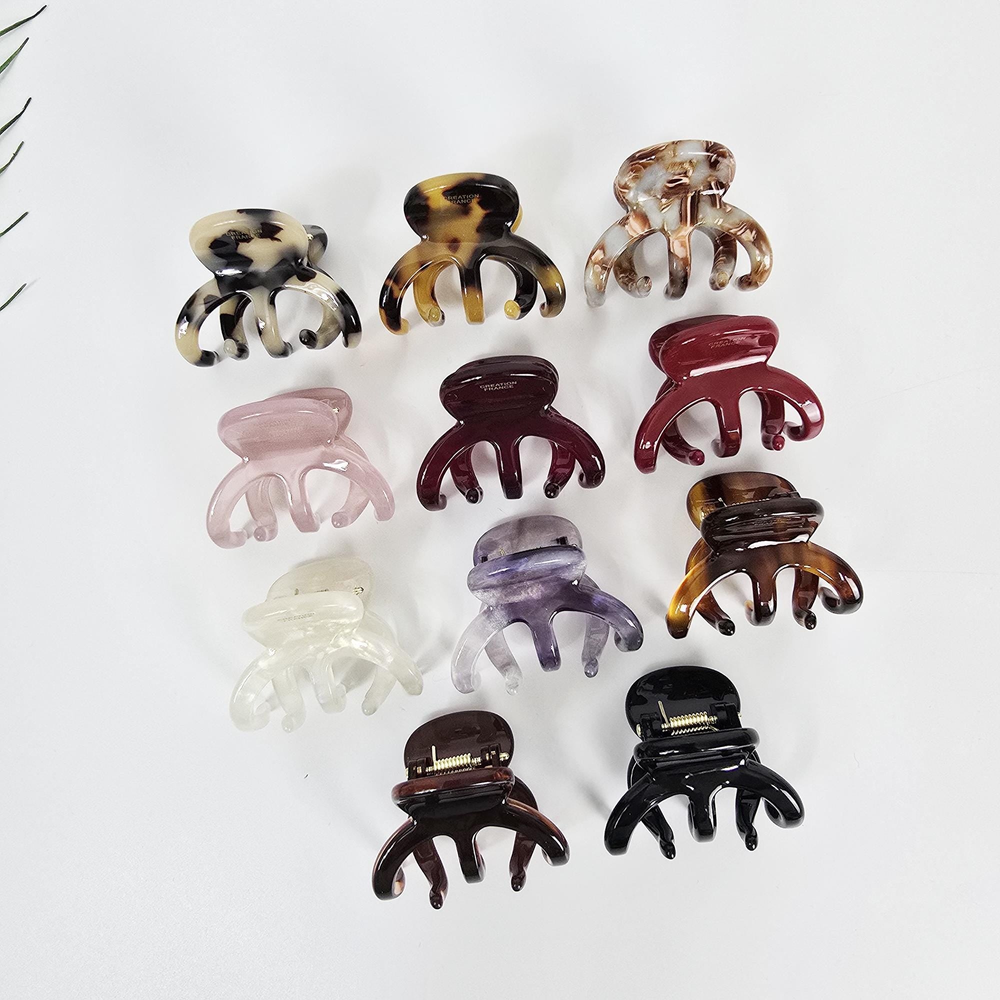 Cellulose acetate pentaclaw hair clip in tortoise shell and solid colors. Small 1.8 inch mini jaw clamp for women half up style. Assortment of ten plastic hair claw clips in various colors and patterns, including brown, white, pink, purple, red, and black. The clips are all in the same style, with a four-pronged design.